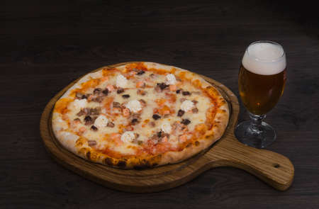 Hot piece of pizza with melted cheese on a rustic wooden table and beer.の写真素材