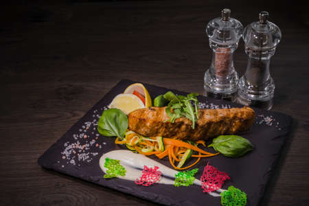 Salmon steak with lemon greens and sauce on stone with salt.の写真素材