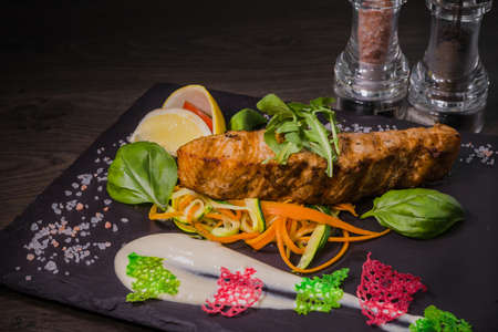 Salmon steak with lemon greens and sauce on stone with salt.の写真素材