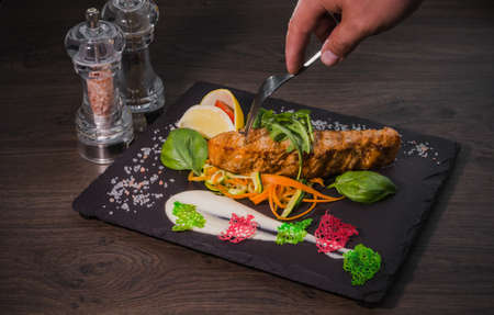 Salmon steak with lemon greens and sauce on stone with salt.の写真素材