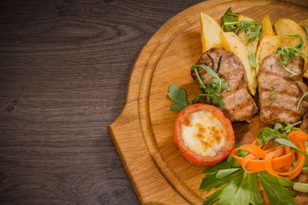 Three pork steaks with fried potatoes and vegetables on a wooden background.の写真素材