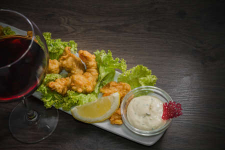 Fried shrimps on a plate with sauce and a glass of wine on a wooden background.の写真素材