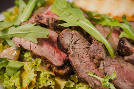 Roasted meat with blood in a cut with vegetables on a wooden background.