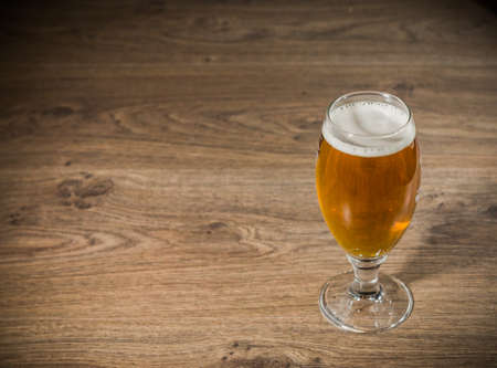 A glass of beer with foam on a wooden background.の写真素材