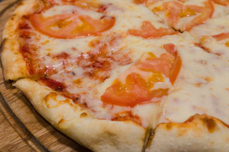 Hot piece of pizza with melted cheese on a rustic wooden table.の写真素材