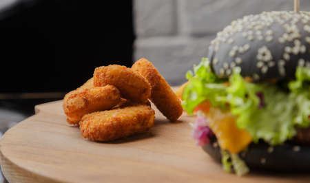 Black burger on a wooden background with potatoes and sauceの写真素材