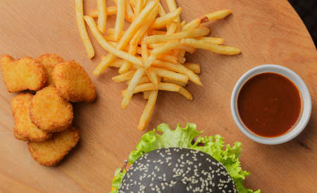 Black burger on a wooden background with potatoes and sauceの写真素材