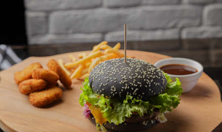 Black burger on a wooden background with potatoes and sauceの写真素材