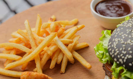 Black burger on a wooden background with potatoes and sauceの写真素材