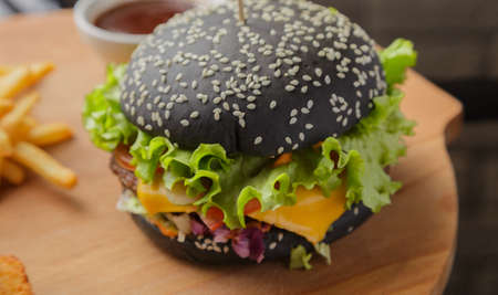 Black burger on a wooden background with potatoes and sauceの写真素材