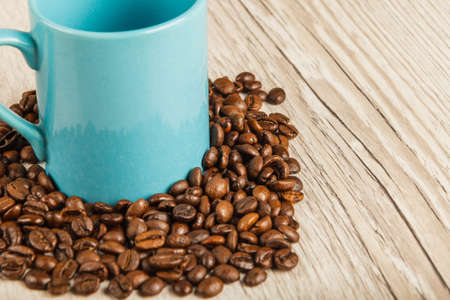 Grains of coffee on a wooden background in large quantities and a cup.