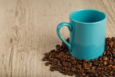 Grains of coffee on a wooden background in large quantities and a cup.の写真素材