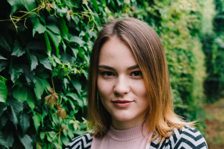 Portrait of a stylish woman against a green foliage background.