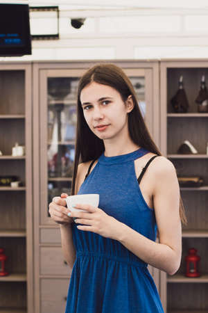 A very beautiful business woman sits in a cafe and holds a cup of coffee in her hands