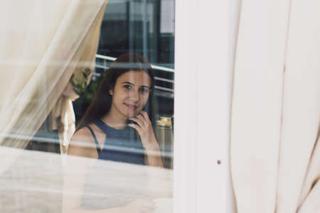 A very beautiful business woman sits in a cafe and holds a cup of coffee in her hands behind a glass