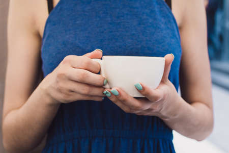A very beautiful business woman sits in a cafe and holds a cup of coffee in her handsの写真素材