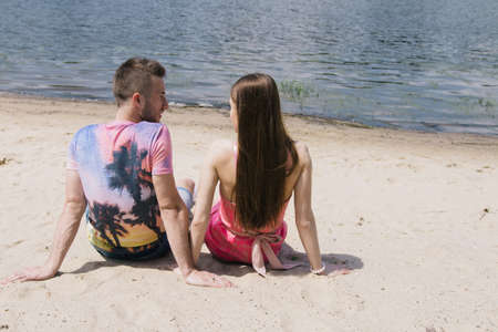 Young couple hugging and smiling at each other on the river bank. Walking along the sandy beach
