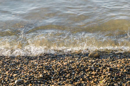 pebbles on the beach pebbles on the sea shore and waves of water illuminated by the rays of the sunの写真素材