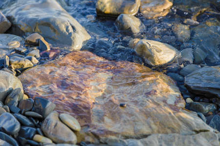 pebbles on the beach pebbles on the sea shore and waves of water illuminated by the rays of the sun.