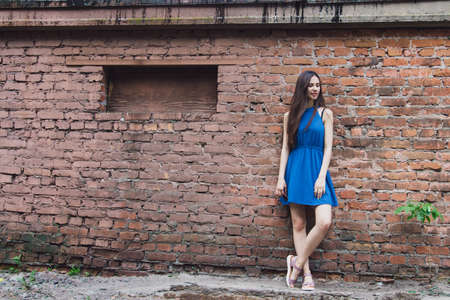 A very beautiful and cheerful girl stands on the street near a brick wallの写真素材