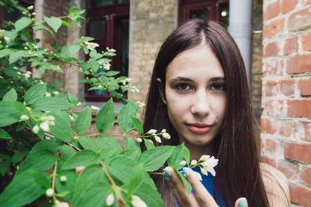 A very beautiful and cheerful girl stands on the street near a bush with white flowersの写真素材