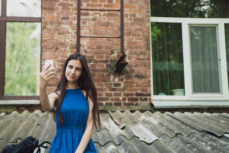 A very beautiful and cheerful girl stands on the street with long, luxurious hair and makes a selfie