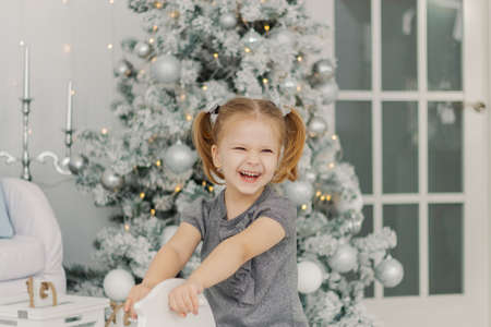 beautiful little girl in a white dress like a princess is sitting on a toy wooden horse in a vintage studio, New Year and Christmas photography.の写真素材