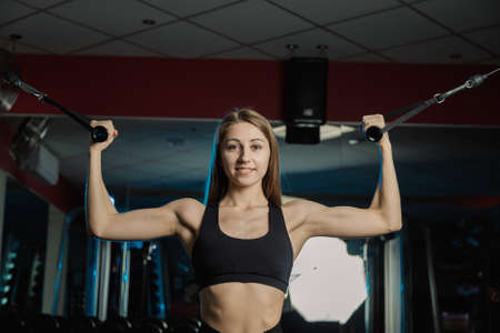 Active beautiful fitness model girl trains biceps on the block in the gym.の写真素材