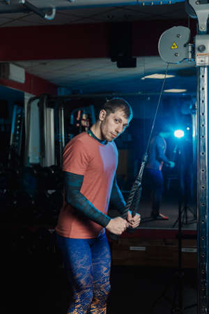 Handsome athletic man trains triceps on the block in the gym.