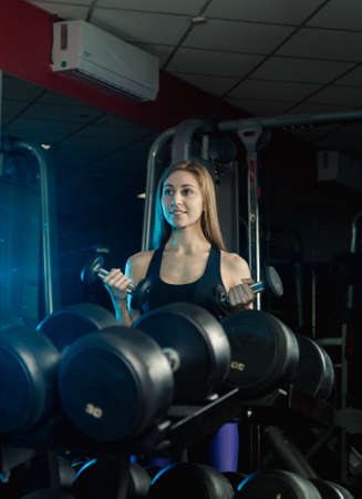 Young and beautiful woman working out with dumbbells in gym. Biceps curls.