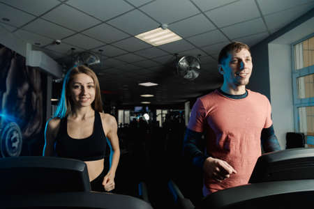 Active beautiful fitness model girl and athletic man train on the treadmill in the gym.