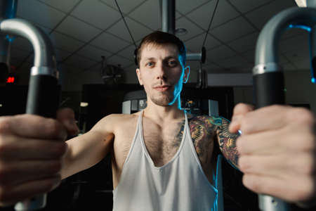 Handsome athletic man trains pectoral muscles on a simulator in the gym.