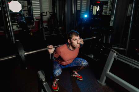 Handsome athletic man doing a squat in the gym.