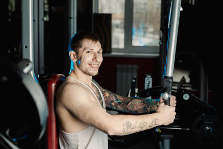 Handsome athletic man trains pectoral muscles on a simulator in the gym.