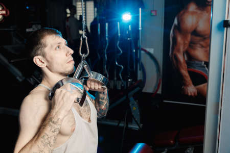 Handsome athletic man working out on the gym machine in the gym.