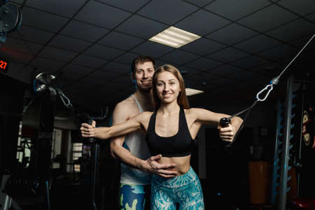 Active beautiful fitness model girl trains the pectoral muscles on the simulator along with a...