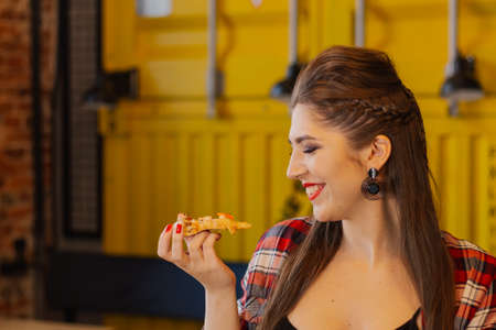 Beautiful and sexy girl sitting by the window in a cafe and eating pizza.