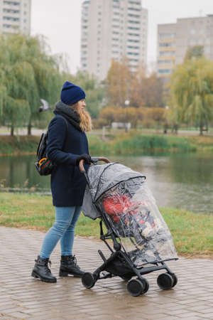 A woman walks in the park with a stroller and a small child near the lake.