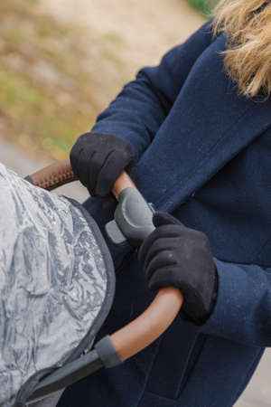 A woman walks in the park with a stroller and a small child.