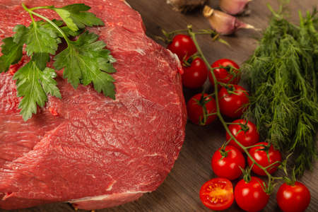 Raw beef on a wooden background with spices and vegetables.