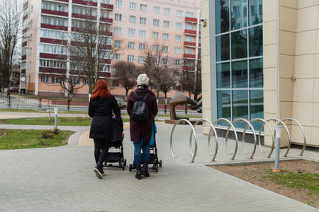 Two mothers walk with baby strollers near the building.の写真素材