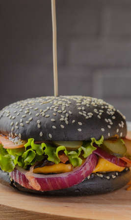 Black burger on a wooden background with potatoes and sauceの写真素材