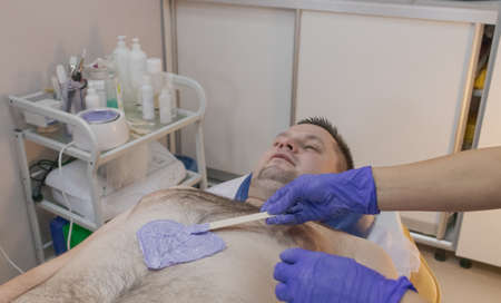 Handsome man on waxing procedure in a beauty salon.の写真素材