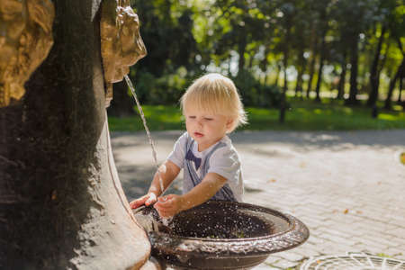 Beautiful little boy plays with a stream of water in the park.の写真素材
