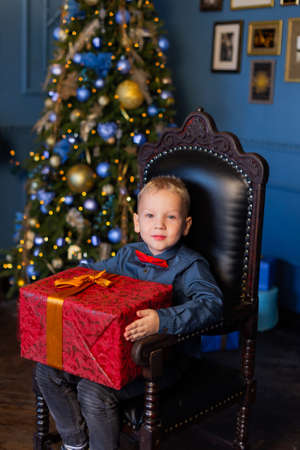 Beautiful boy sits on a chair in New Years decor with a gift in his hands.の写真素材