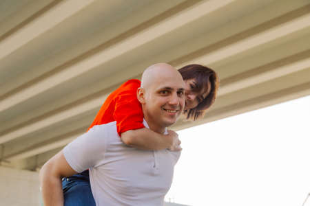 Happy girl on the back of a man at the bridge. Lovers have fun.