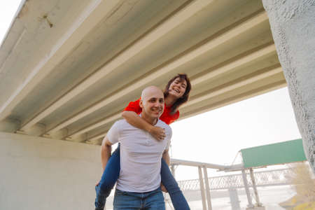 Happy girl on the back of a man at the bridge. Lovers have fun.