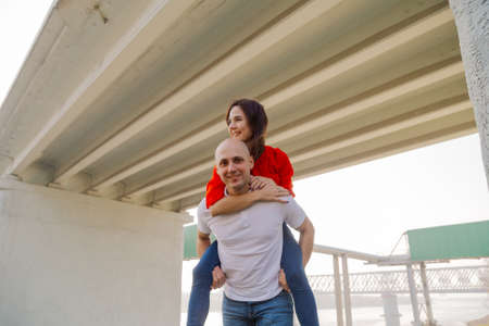 Happy girl on the back of a man at the bridge. Lovers have fun.