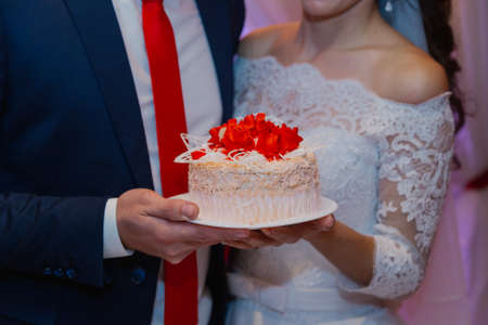 Happy newlyweds hold a wedding cake in their hands