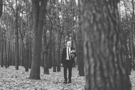 Beautiful happy groom with a bouquet in the autumn forest